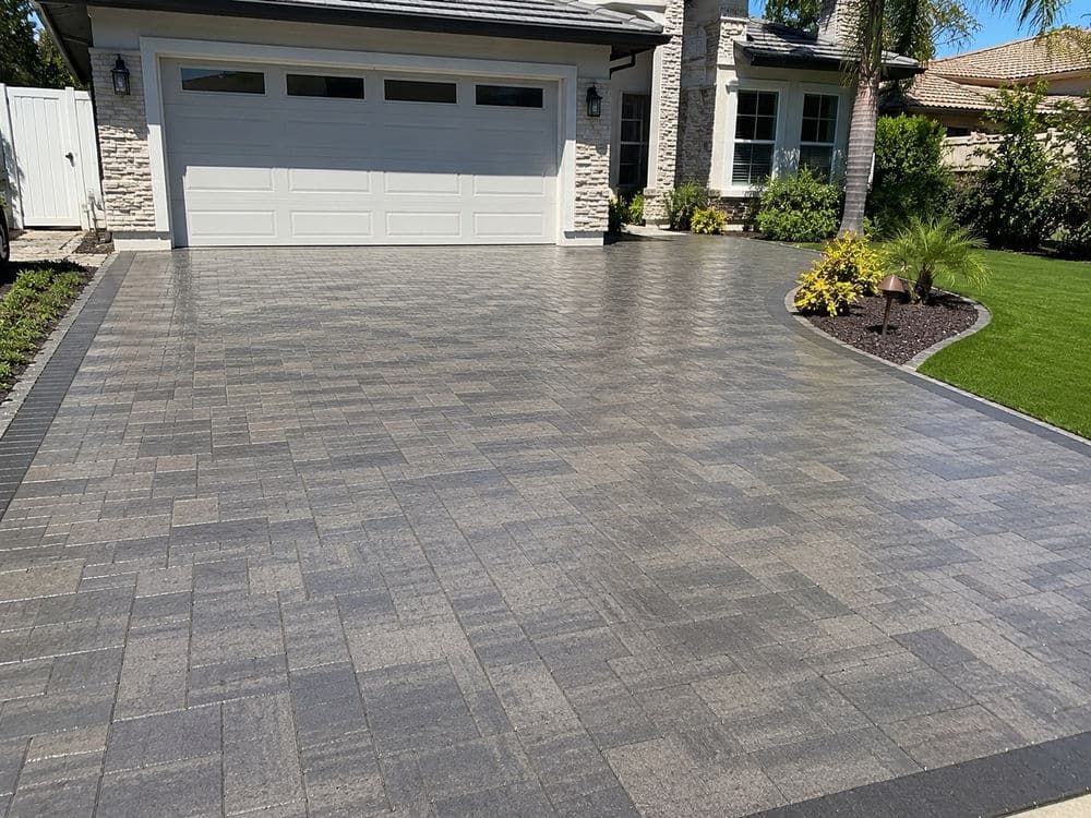 Modern paved driveway with a garage, landscaped greenery, and decorative plants.